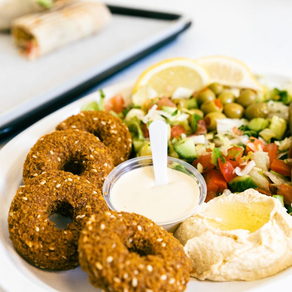 A plate of Casa De Falafel's falafel, hummus, salad, and tahini sauce, with a wrap in the background.