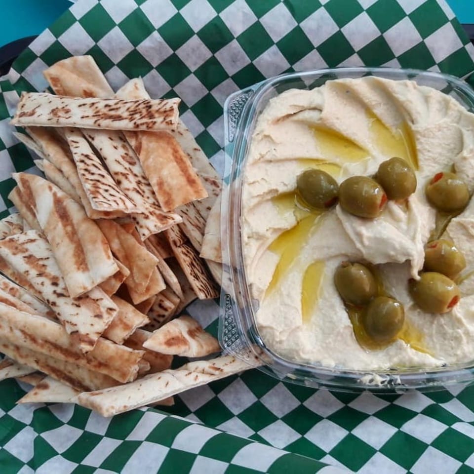 Casa De Falafel's hummus with olive oil and green olives, served with pita bread on checkered paper.