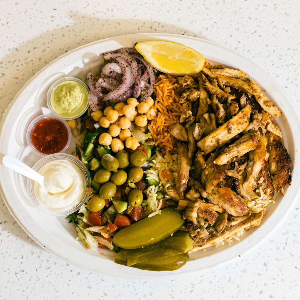 A Casa De Falafel chicken shawarma plate with rice, salad, chickpeas, olives, pickles, and three sauces.