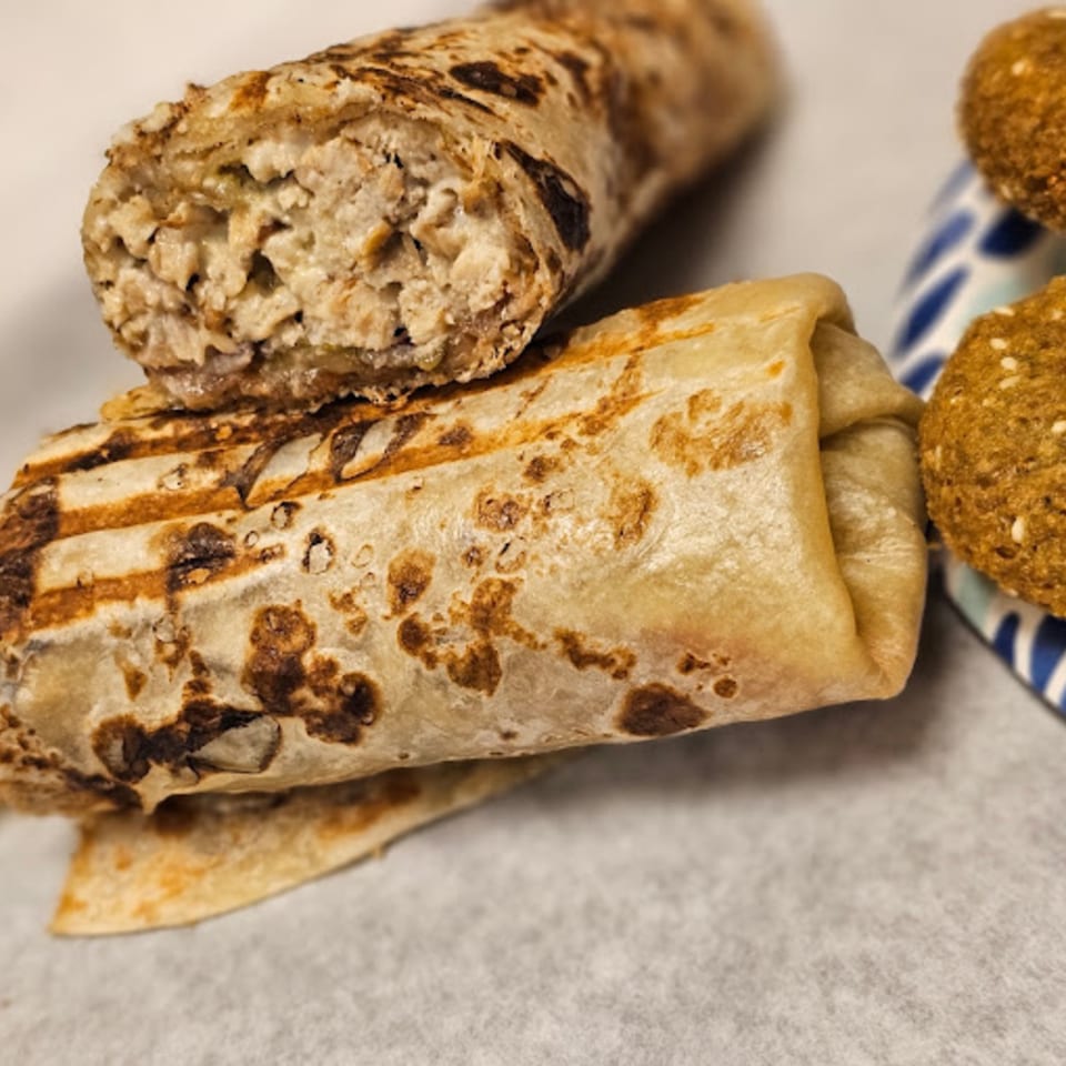 Two grilled falafel wraps, one cut open to show the filling, with falafel balls on a blue plate.