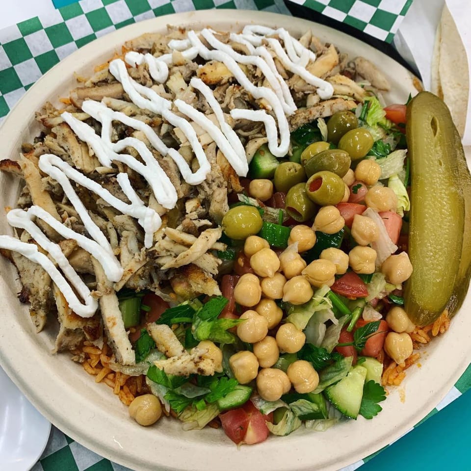 A Casa De Falafel chicken shawarma plate with rice, salad, chickpeas, olives, and a pickle.